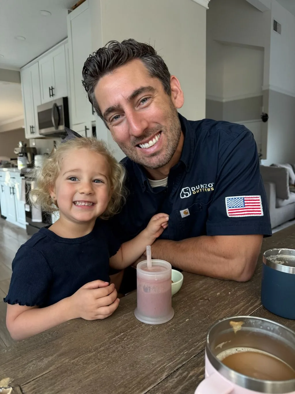 Clark, founder of Dunzo Gutters, smiling with his young daughter in the kitchen