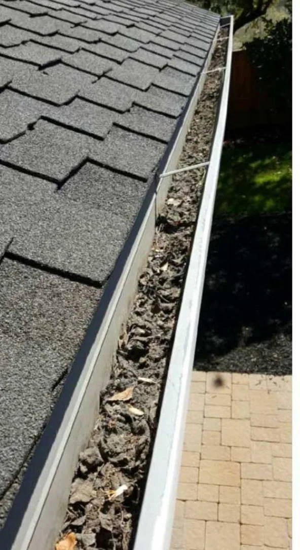 A gutter packed with dark debris on a Sacramento home before cleaning, patio below