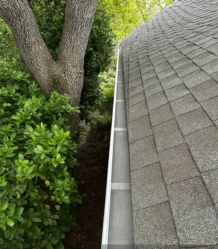 The same gutter clear with micro-mesh guard installed, same trees and hedge