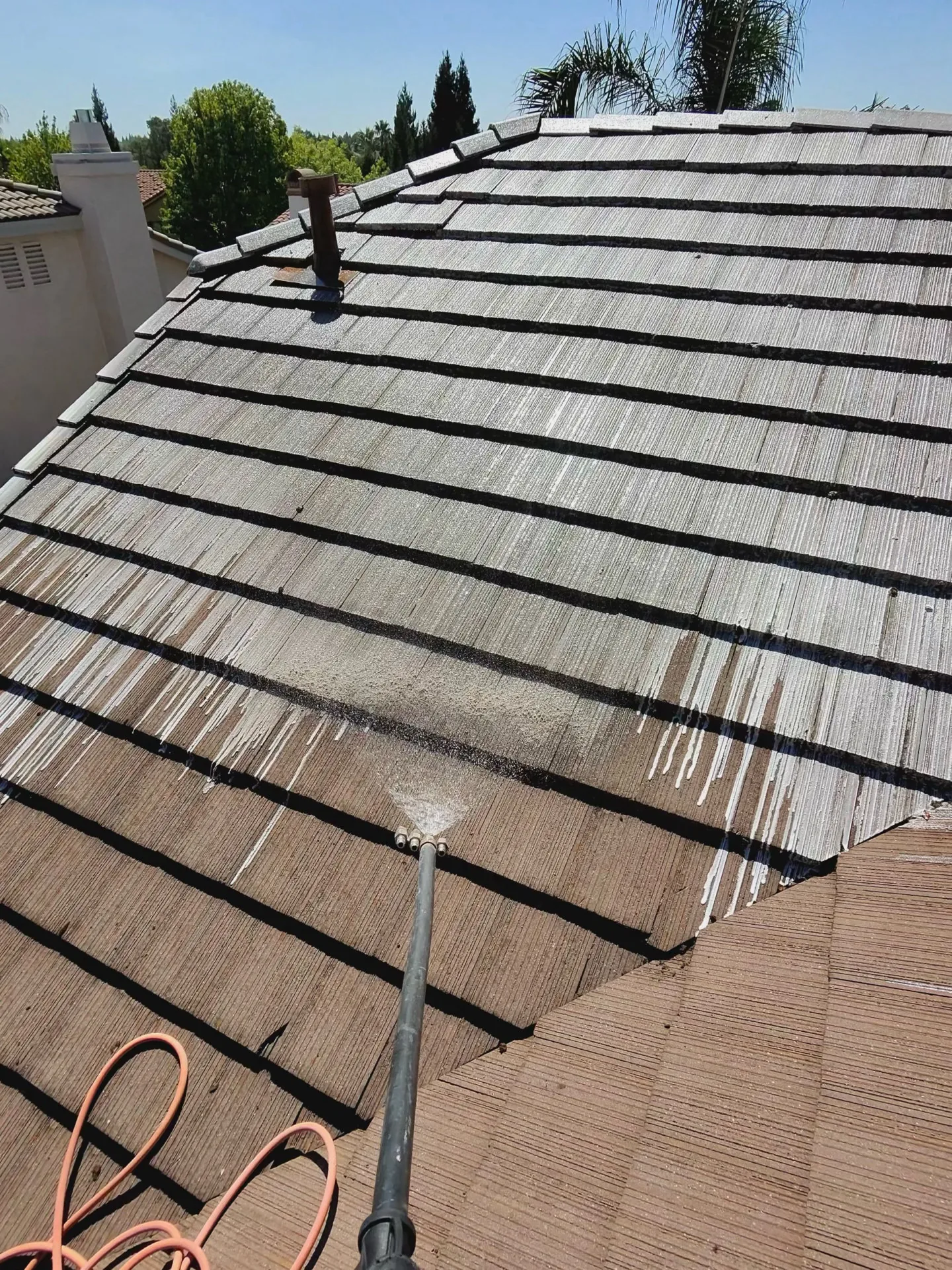 A wand actively soft-washing a tile roof on a Sacramento home, dirty and clean tile visible side by side