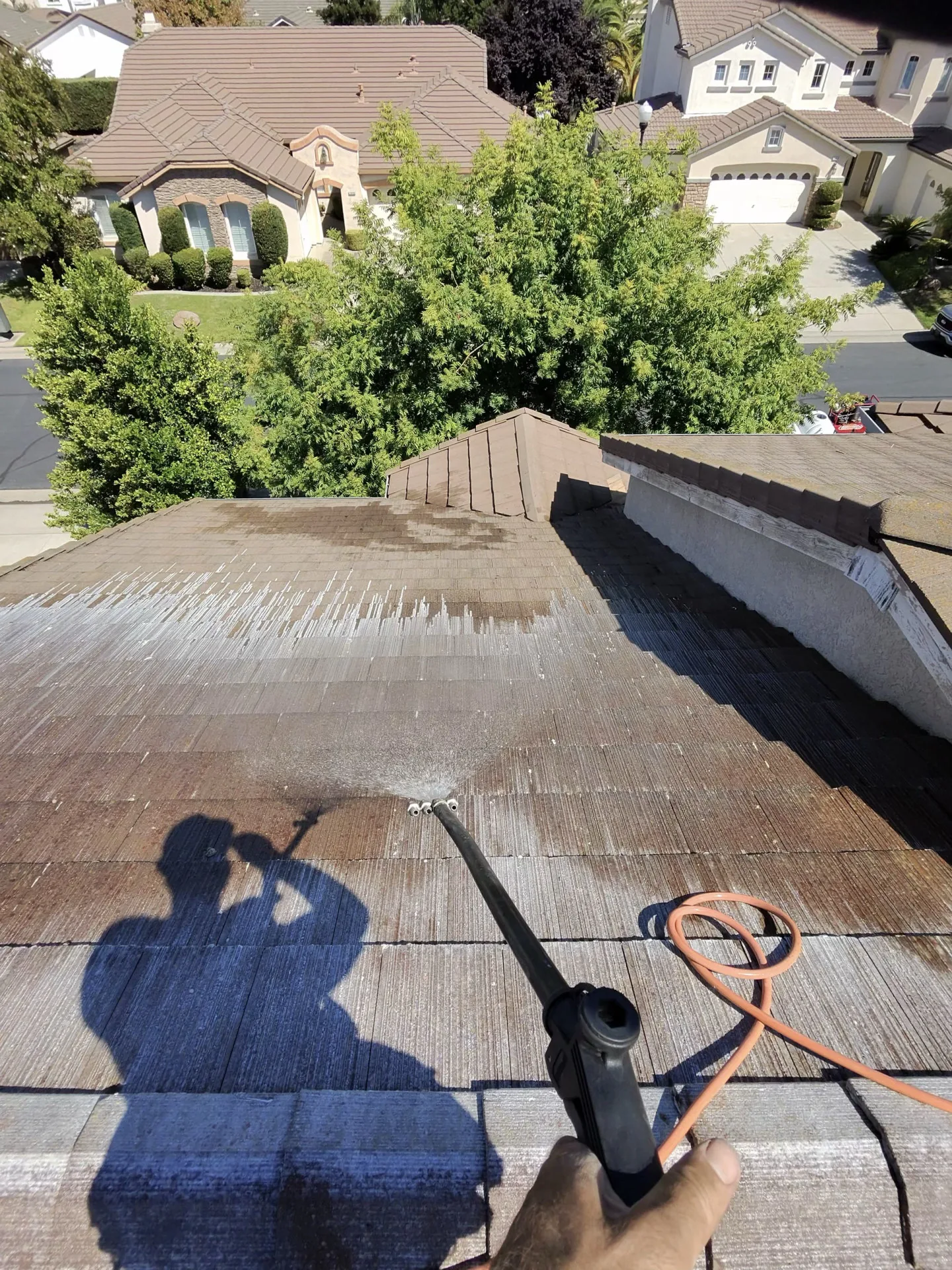 A wand soft-washing a tile roof on a Sacramento home, streaks of clean tile appearing