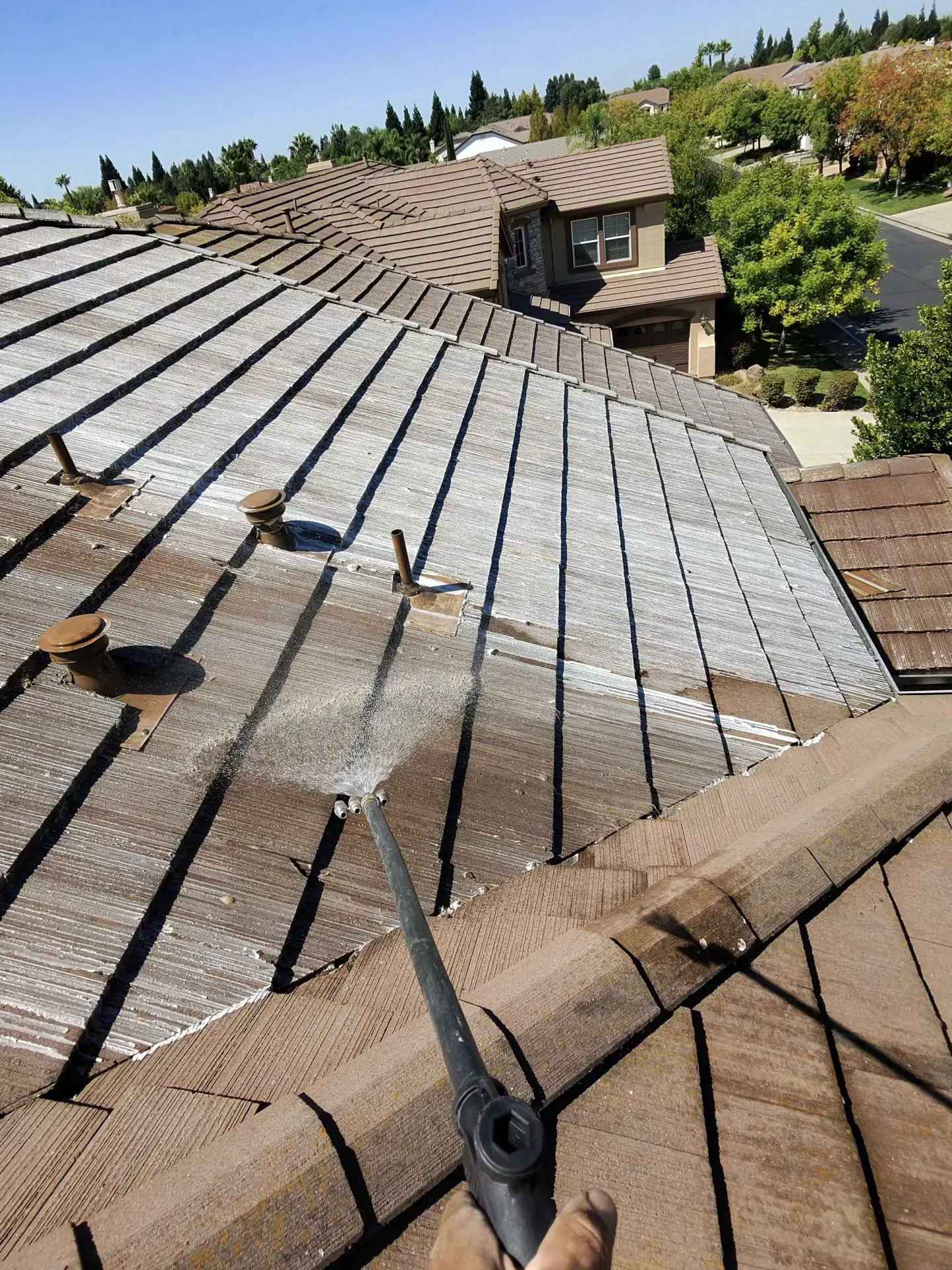 A wand soft-washing a tile roof on a Sacramento home, dirty roof in the background