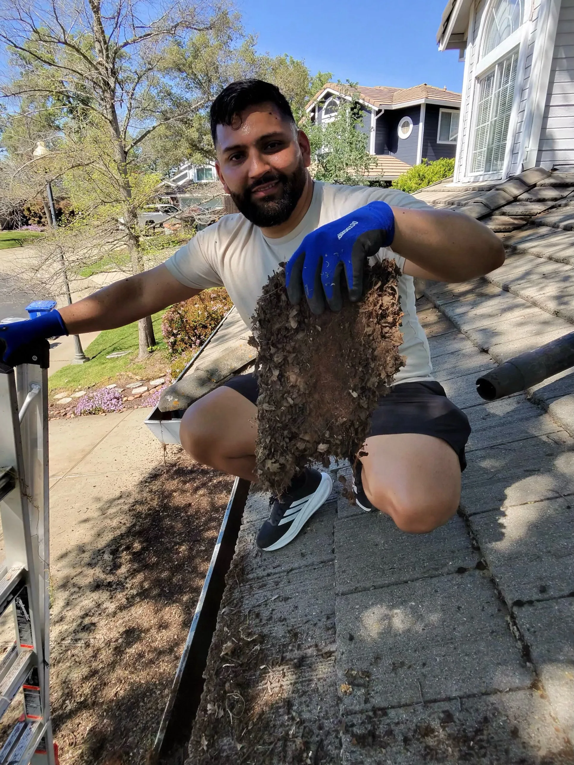 A Dunzo Gutters technician holding up a solid mat of compacted roots and debris pulled from a gutter
