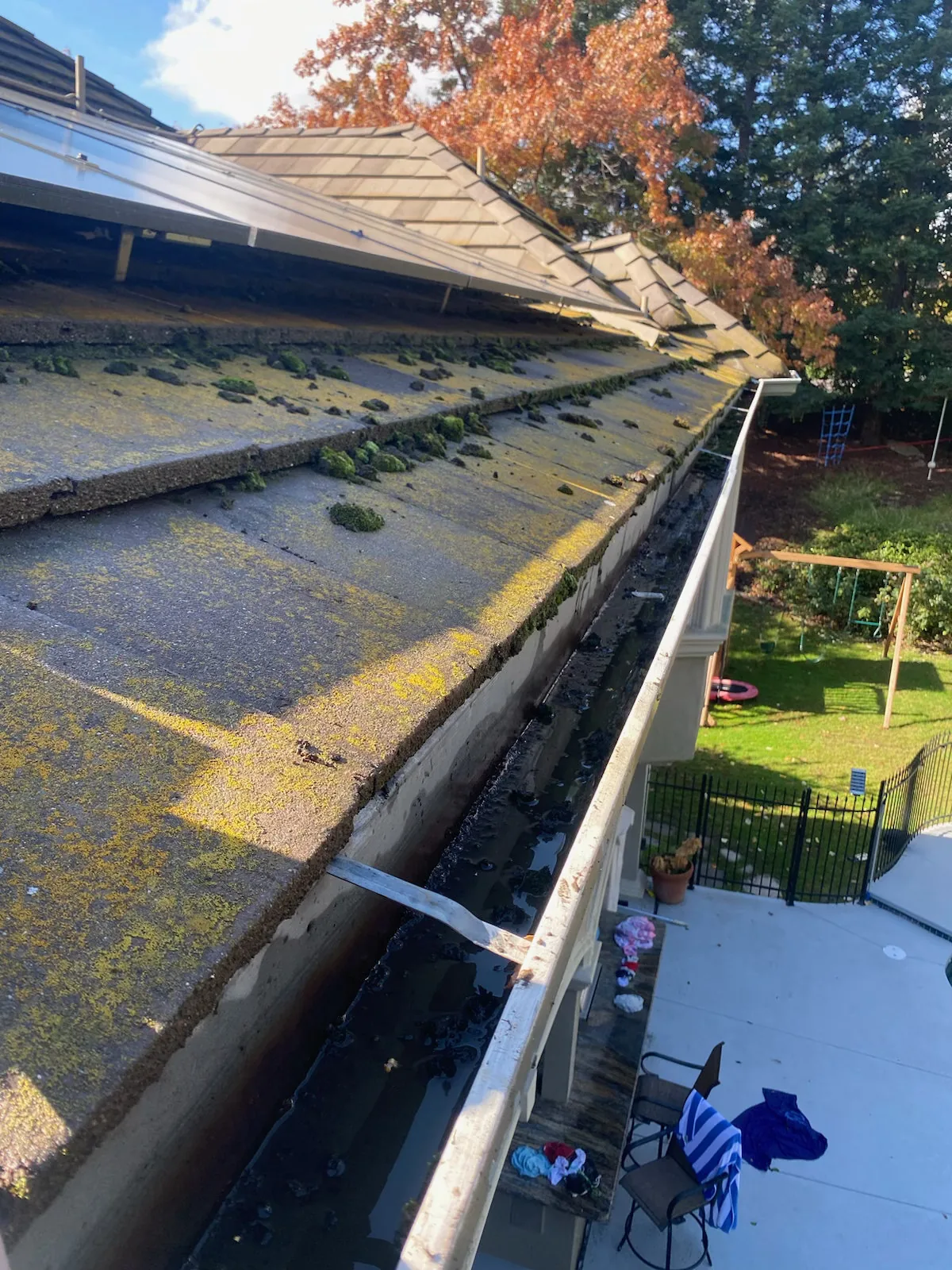 A moss-covered Sacramento roof with a sludge-packed gutter and a lifted solar panel mount before cleaning
