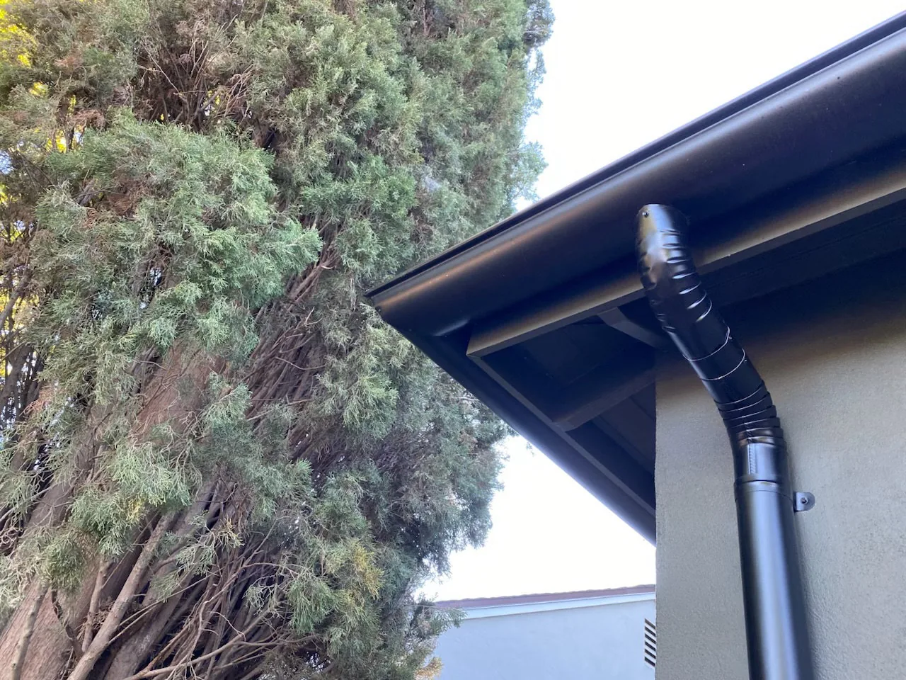 A finished black seamless gutter and downspout on a Sacramento home