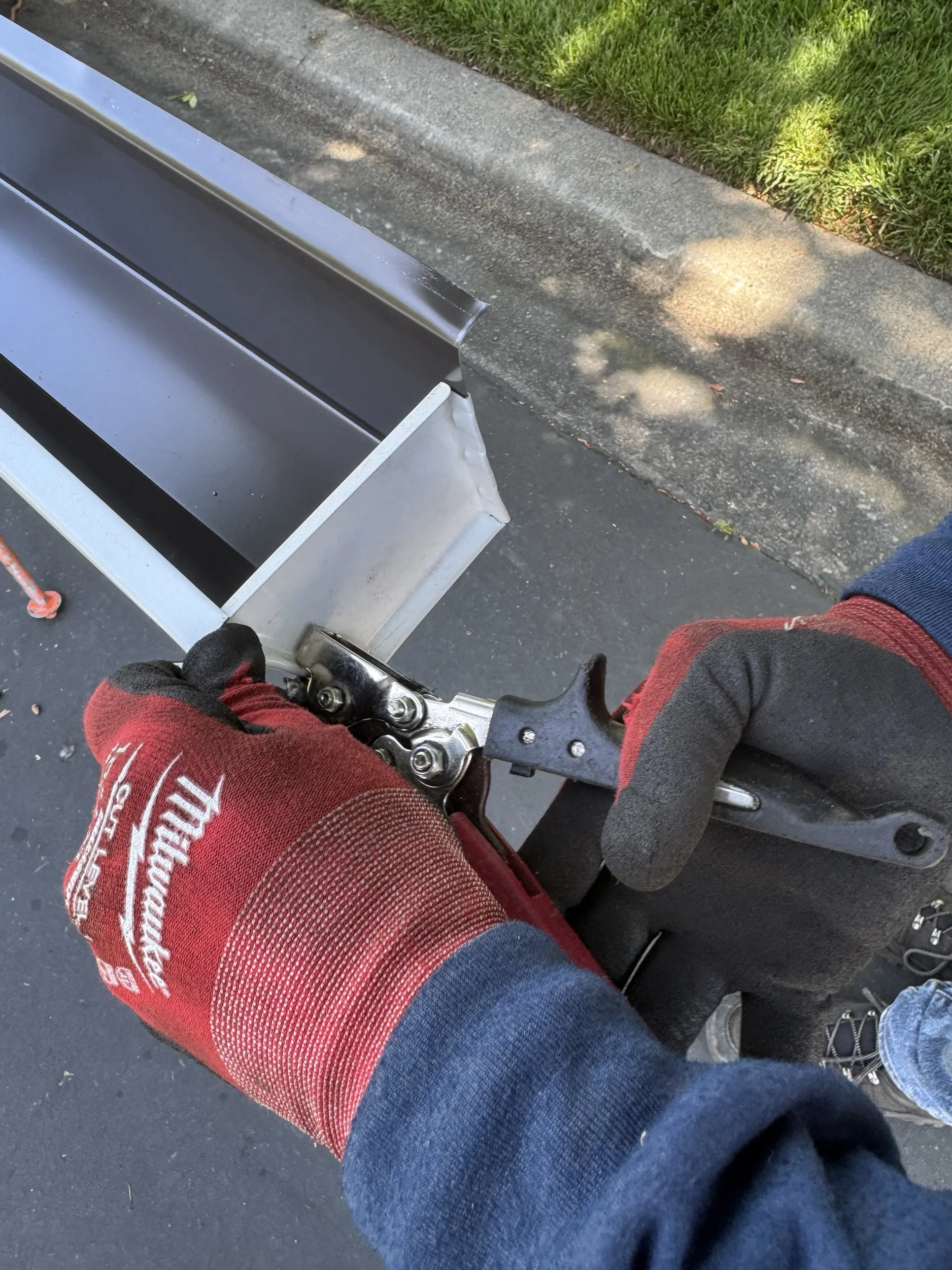 A silver aluminum seamless gutter end cap being crimped into place