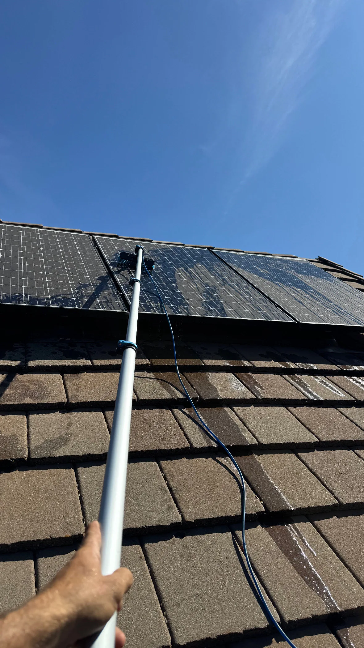 A Dunzo Gutters technician cleaning a solar panel with an extension pole and soft brush